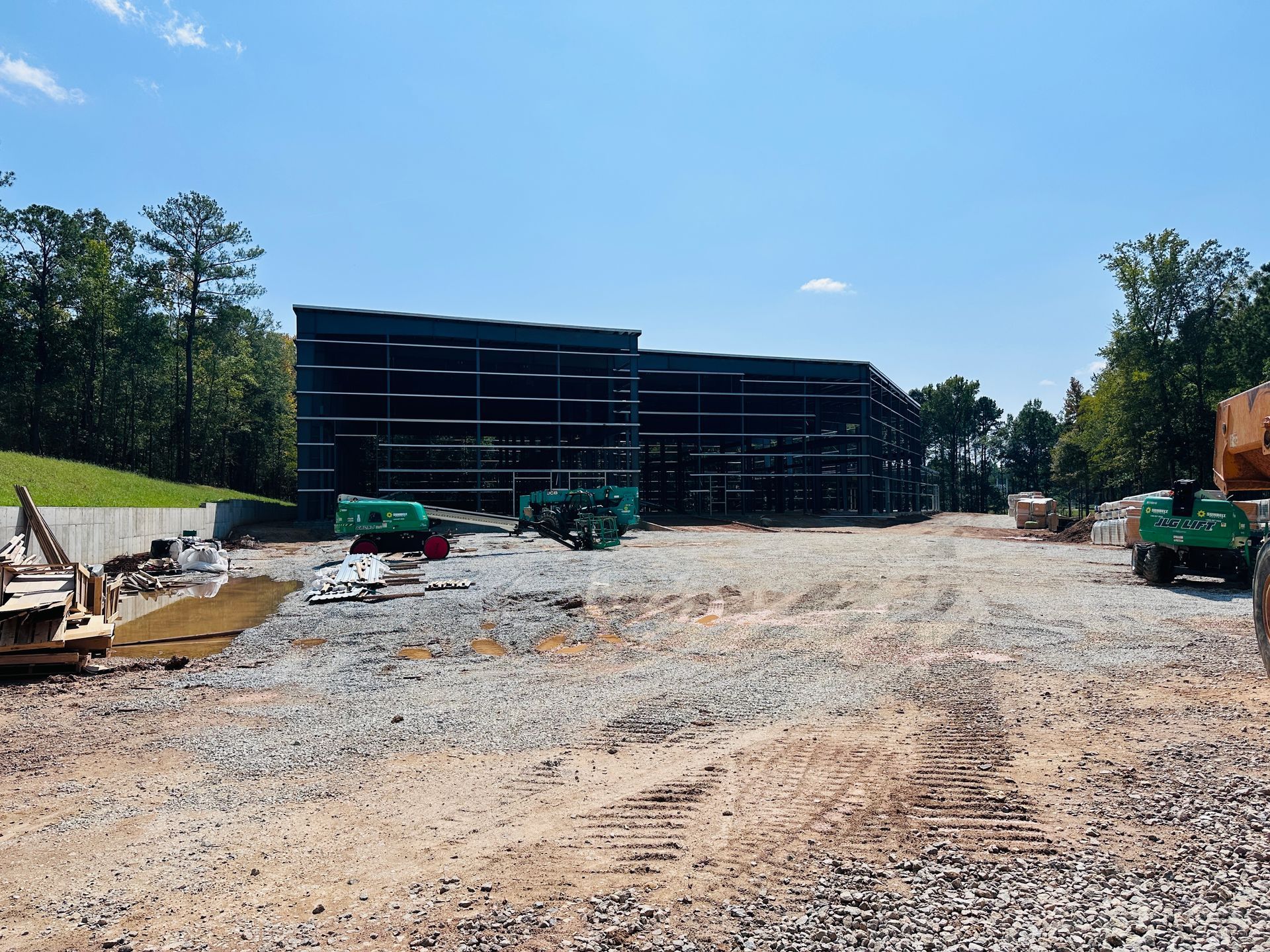 Construction site with unfinished building, gravel lot, and heavy machinery under a clear blue sky