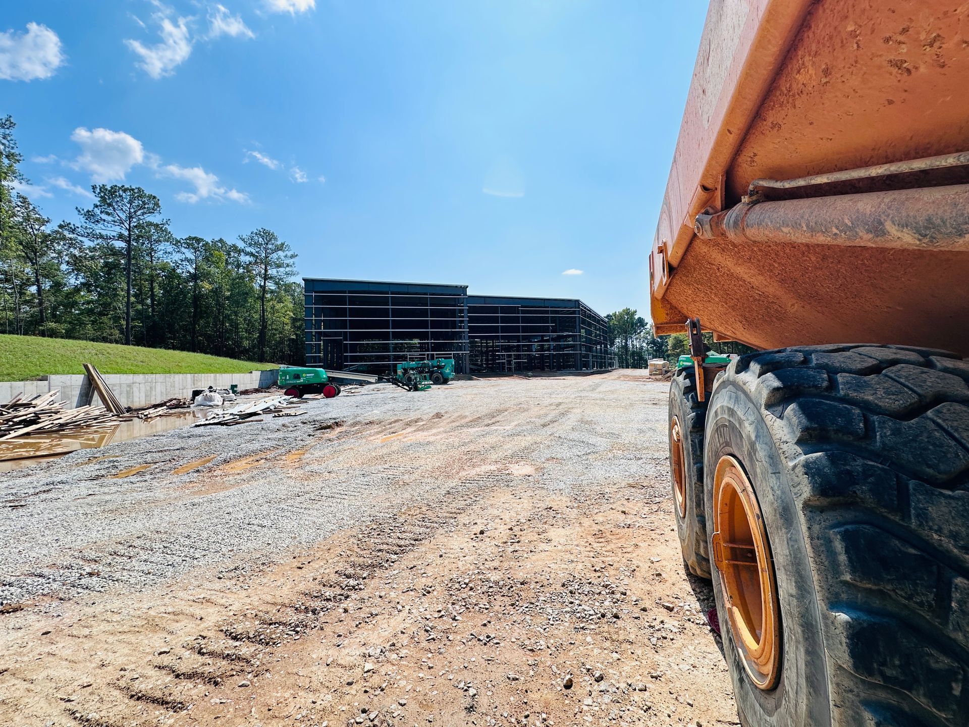 Gravel road at a construction site with a large earth mover in the foreground and equipment ahead under a blue sky