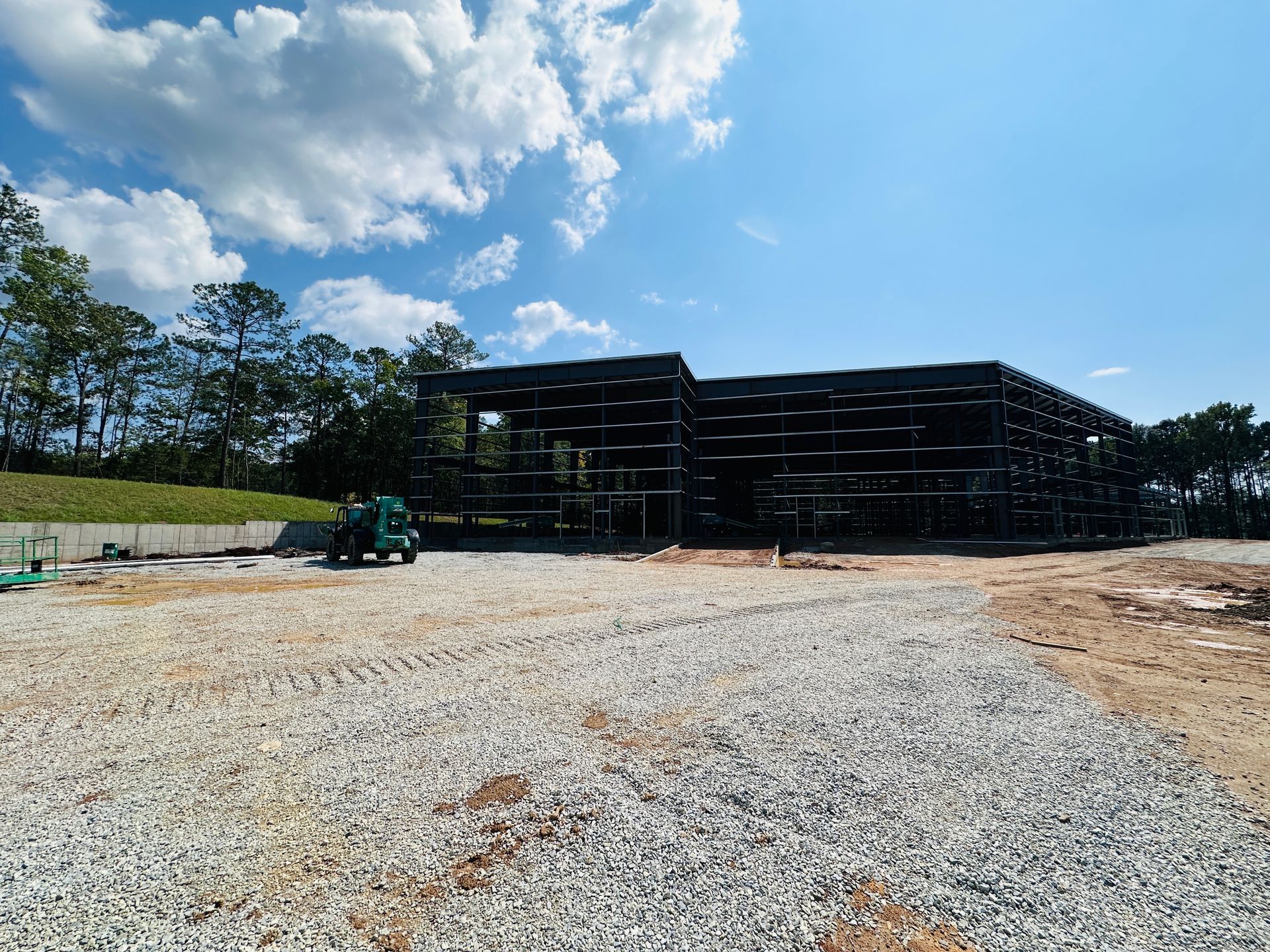 Construction site with gravel foreground, black building frame, and blue sky with clouds