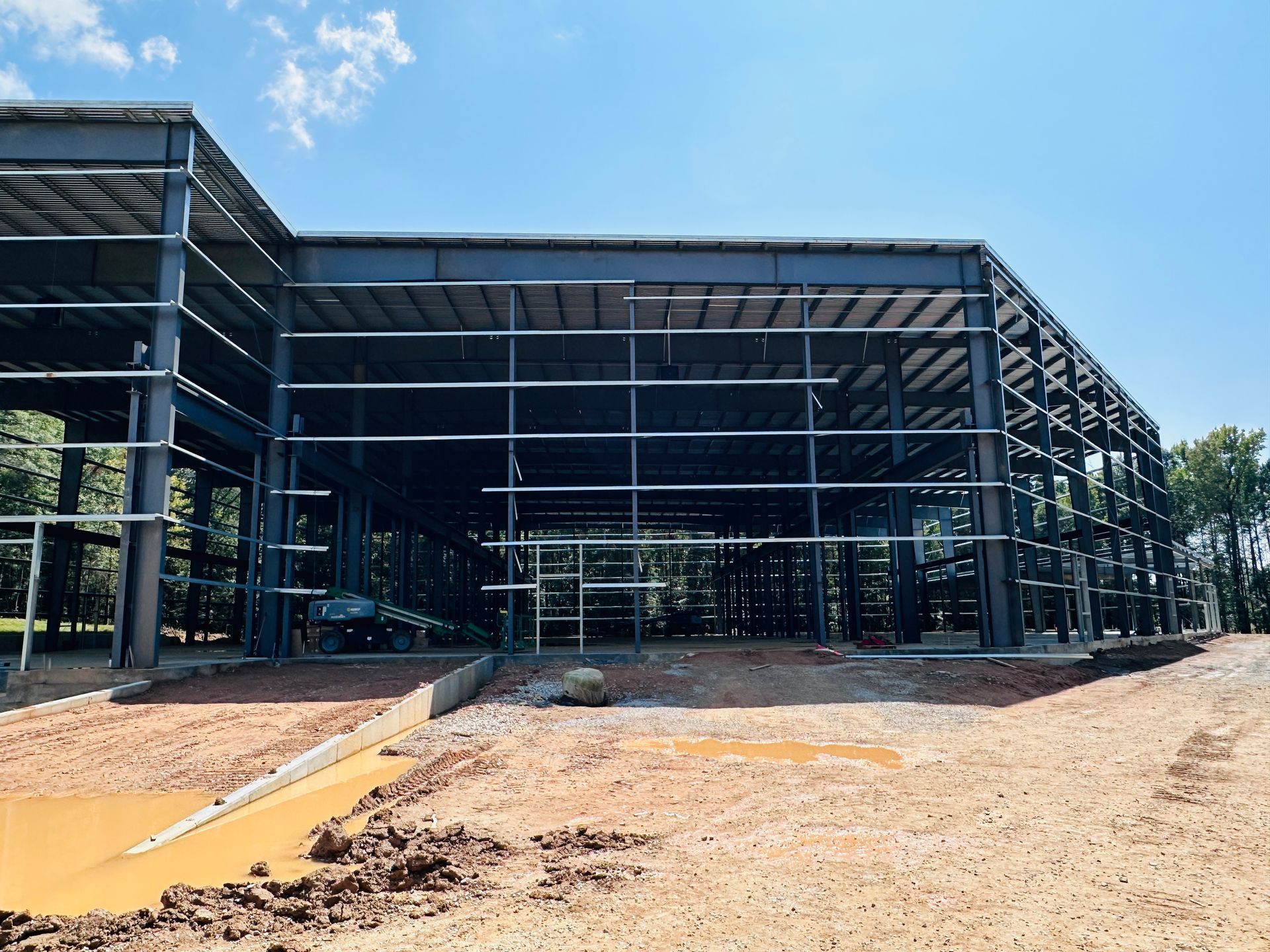 Steel-framed building under construction with an orange dirt path and blue sky