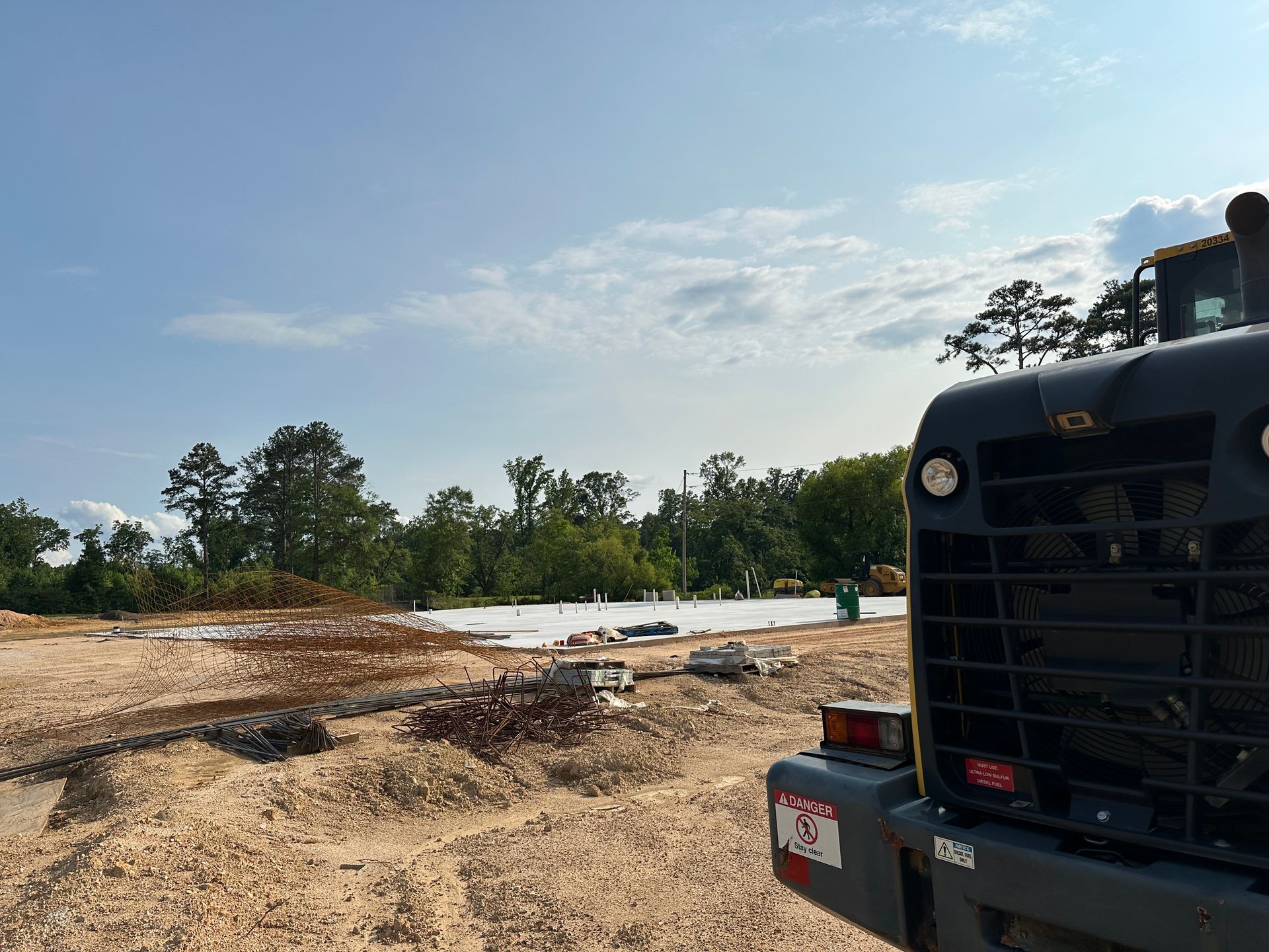 Bulldozer on a muddy construction site with trees and a bright sky in the background