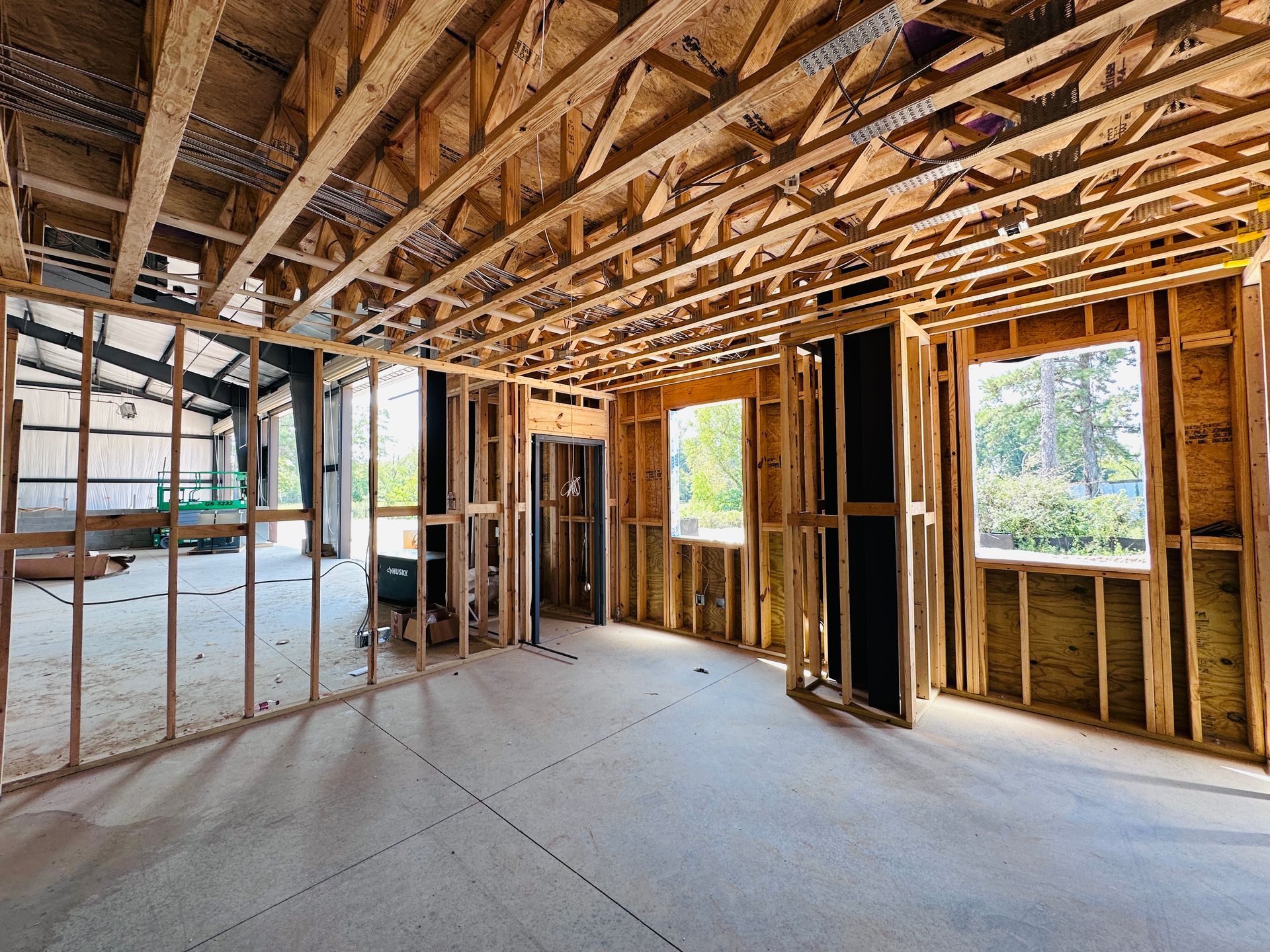 Unfinished house interior with exposed wooden framing, open windows, and a concrete floor