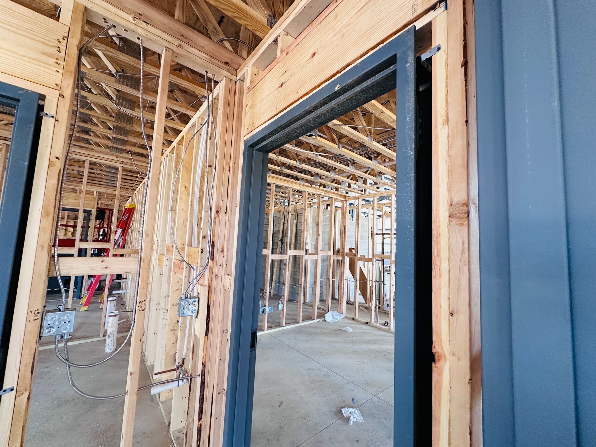 Interior of a house under construction with exposed framing, drywall, and a blue exterior wall beside a doorway