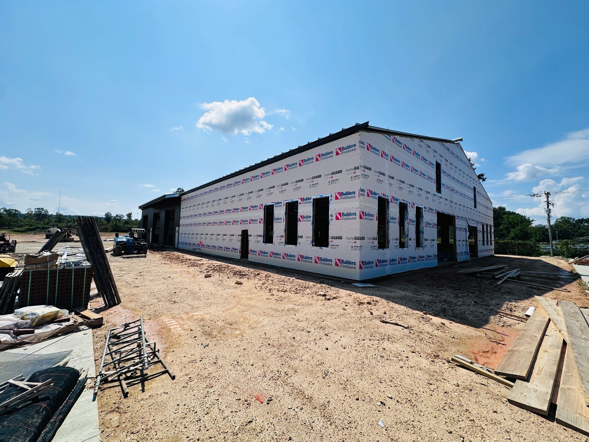 Construction site with a partially built white-wrapped building and dirt lot under a blue sky