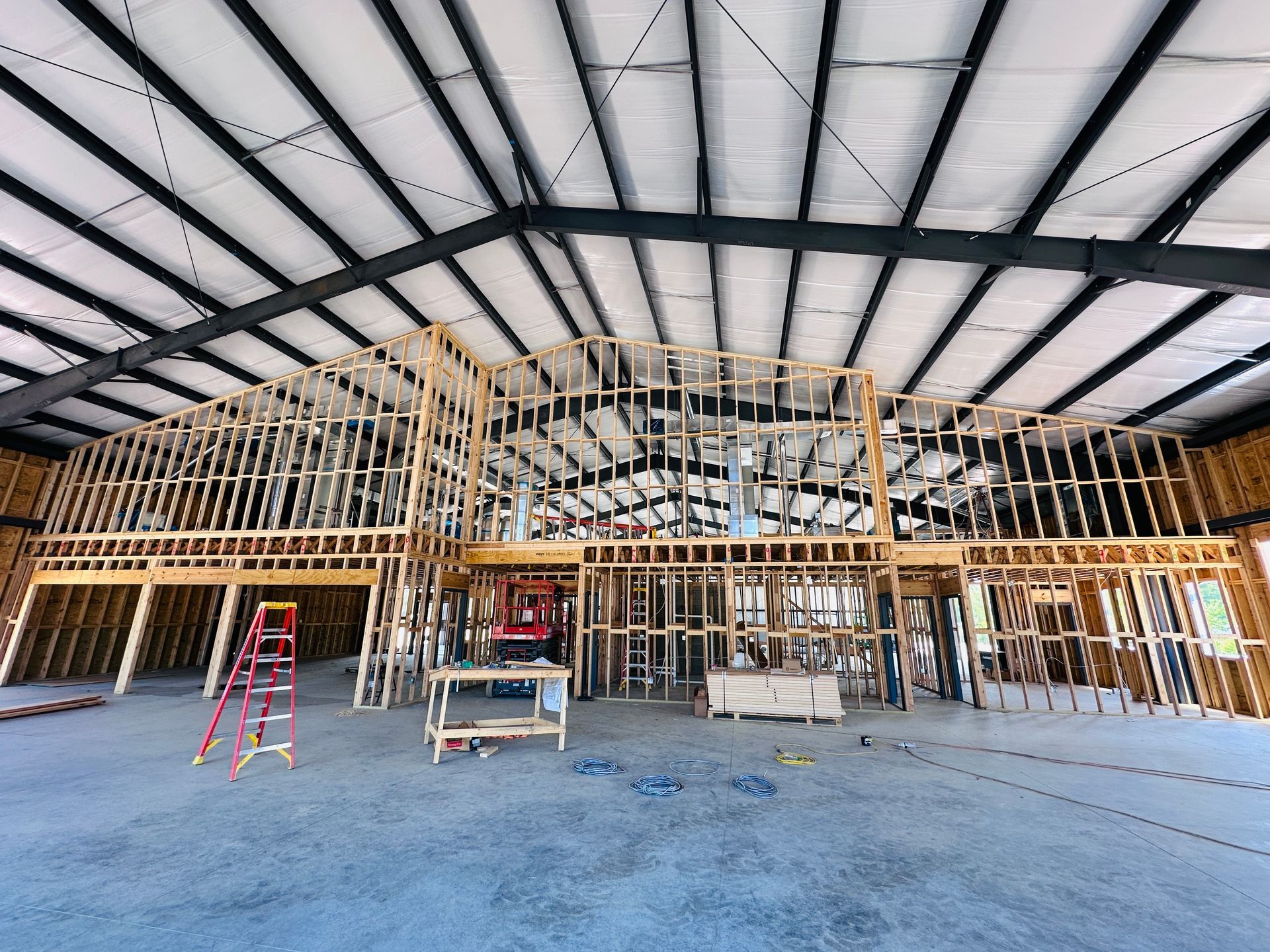 Large unfinished building interior with wooden framing, exposed steel roof beams, and construction tools on the floor