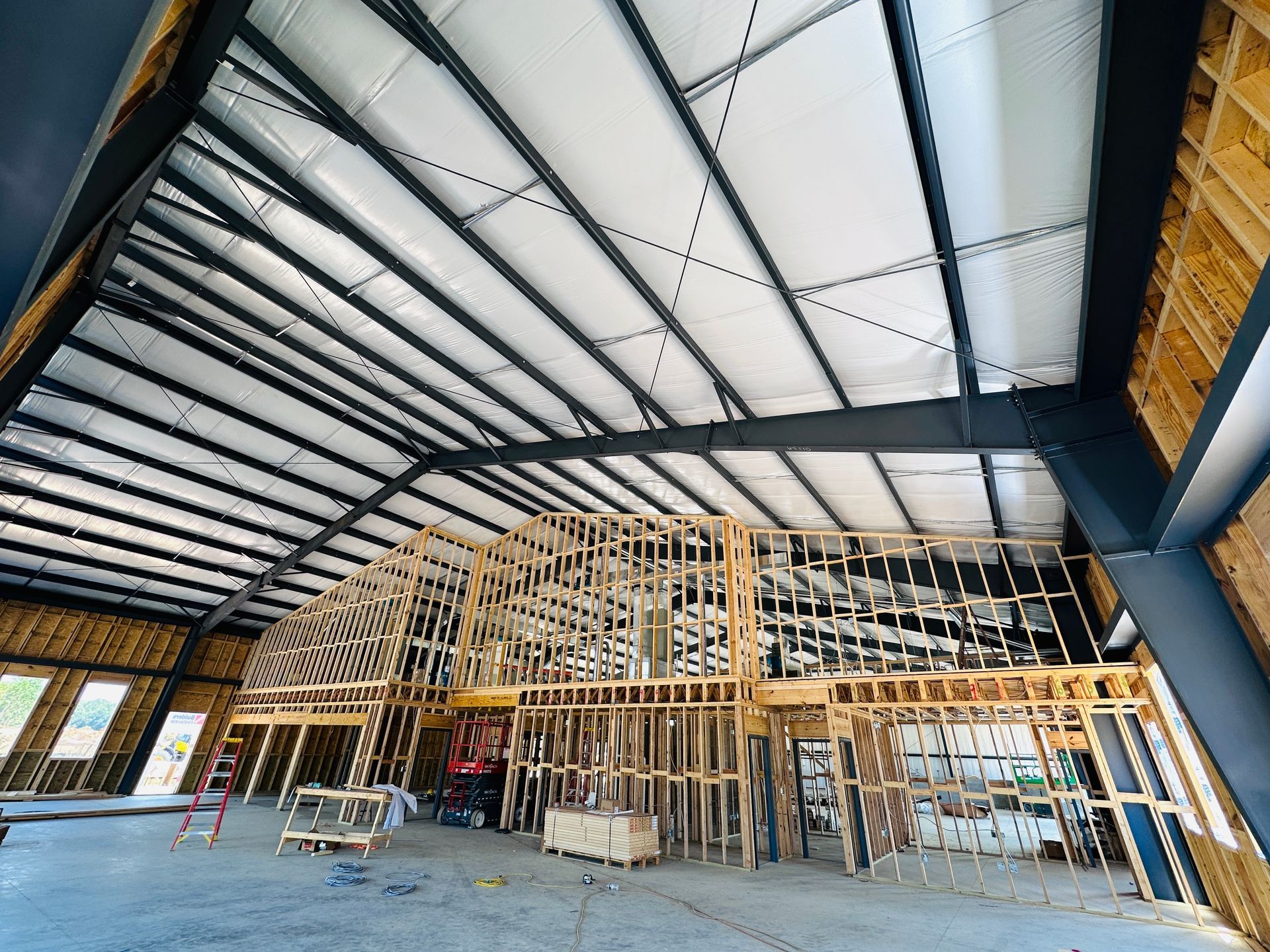 Interior of a building under construction with exposed steel beams and wooden framing under a high ceiling