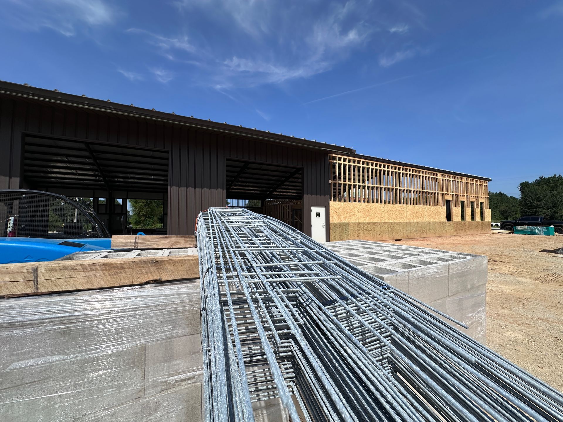Construction site with steel rebar bundle leading toward a partially built wooden structure under a blue sky