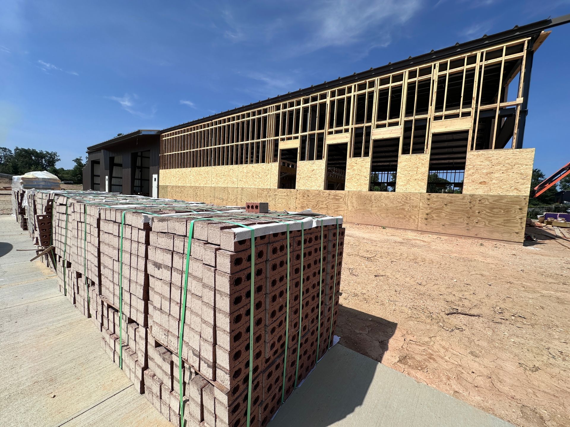 Construction site with stacked bricks in front of a partially framed building under a blue sky