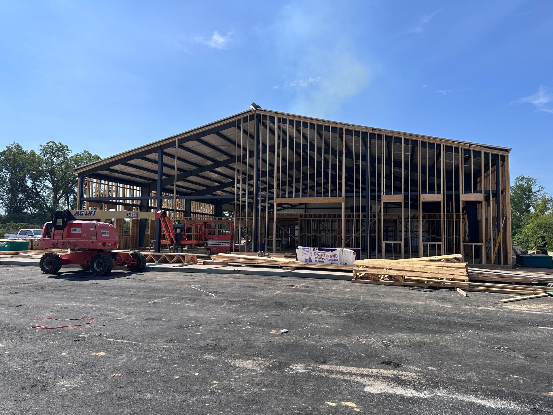 Construction site with steel-framed building under construction, red trucks, and lumber in front