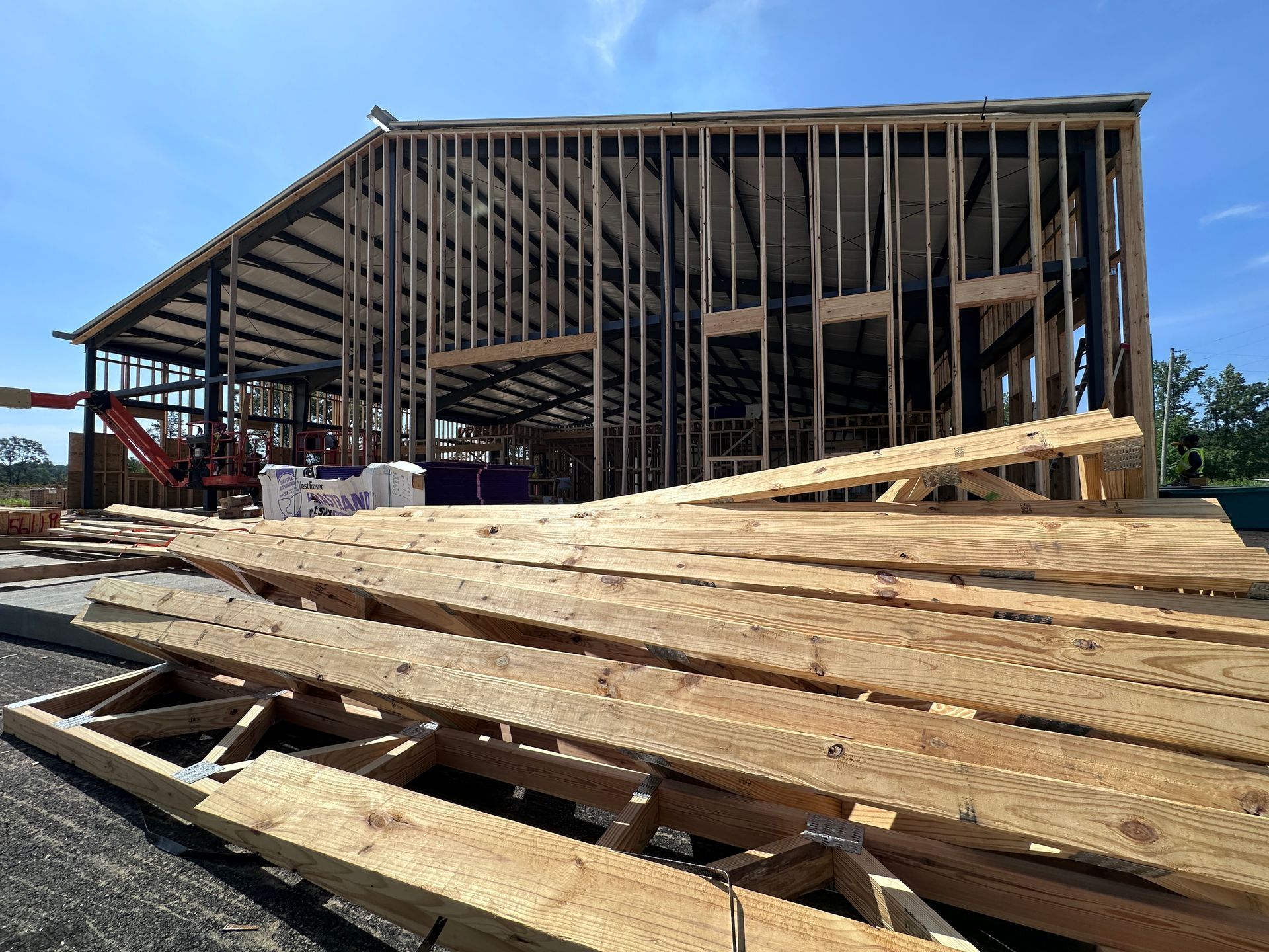 Stacked lumber and a partially framed house under construction on a sunny day