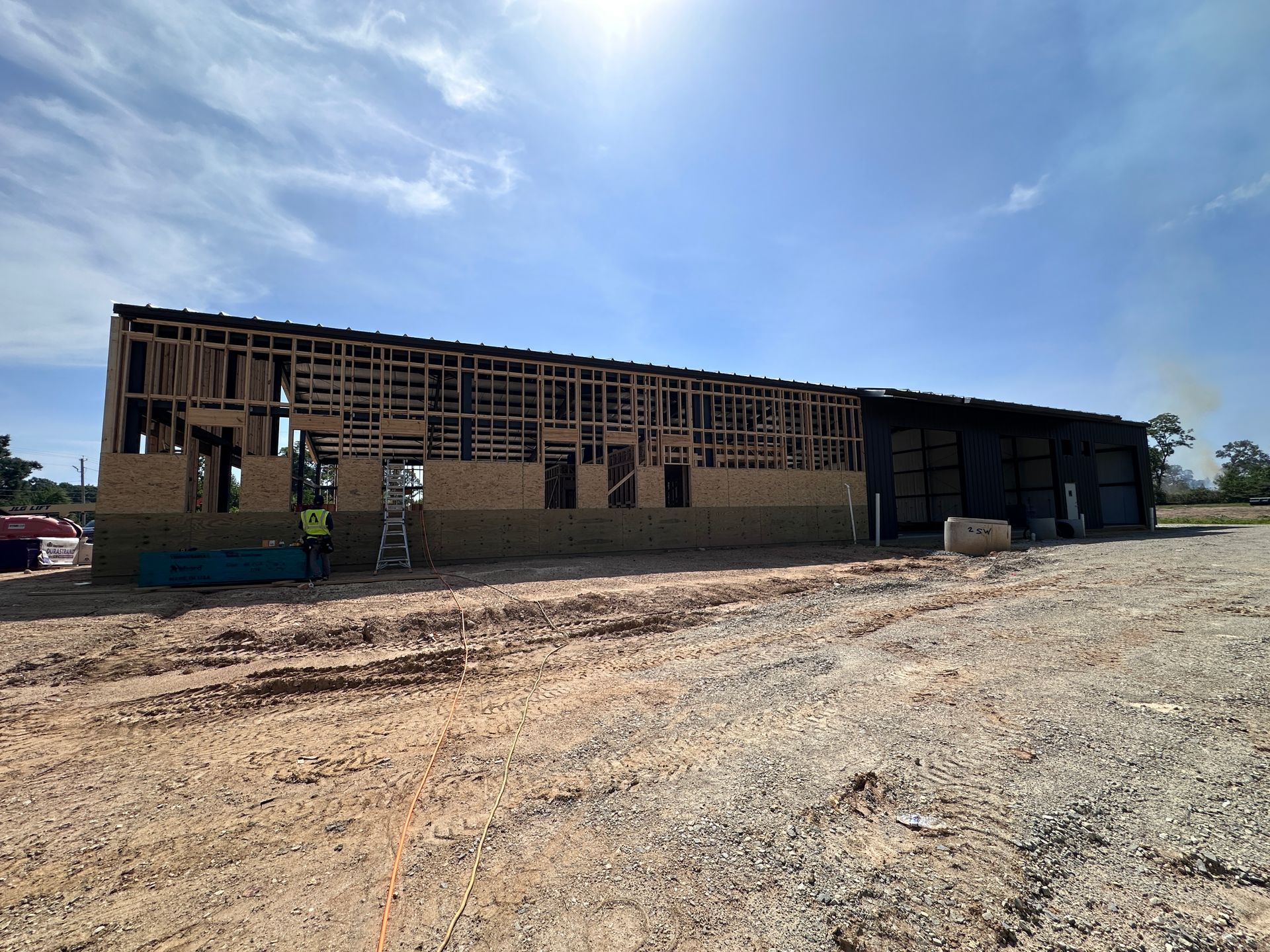 Partially built brick building with workers on a dusty construction site under a bright blue sky