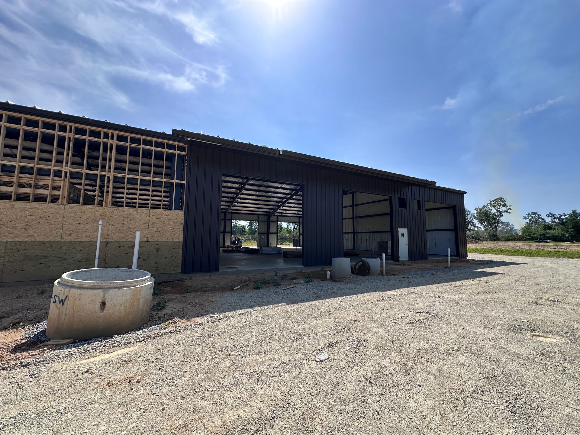 Partially built metal barn on a gravel lot under a bright blue sky