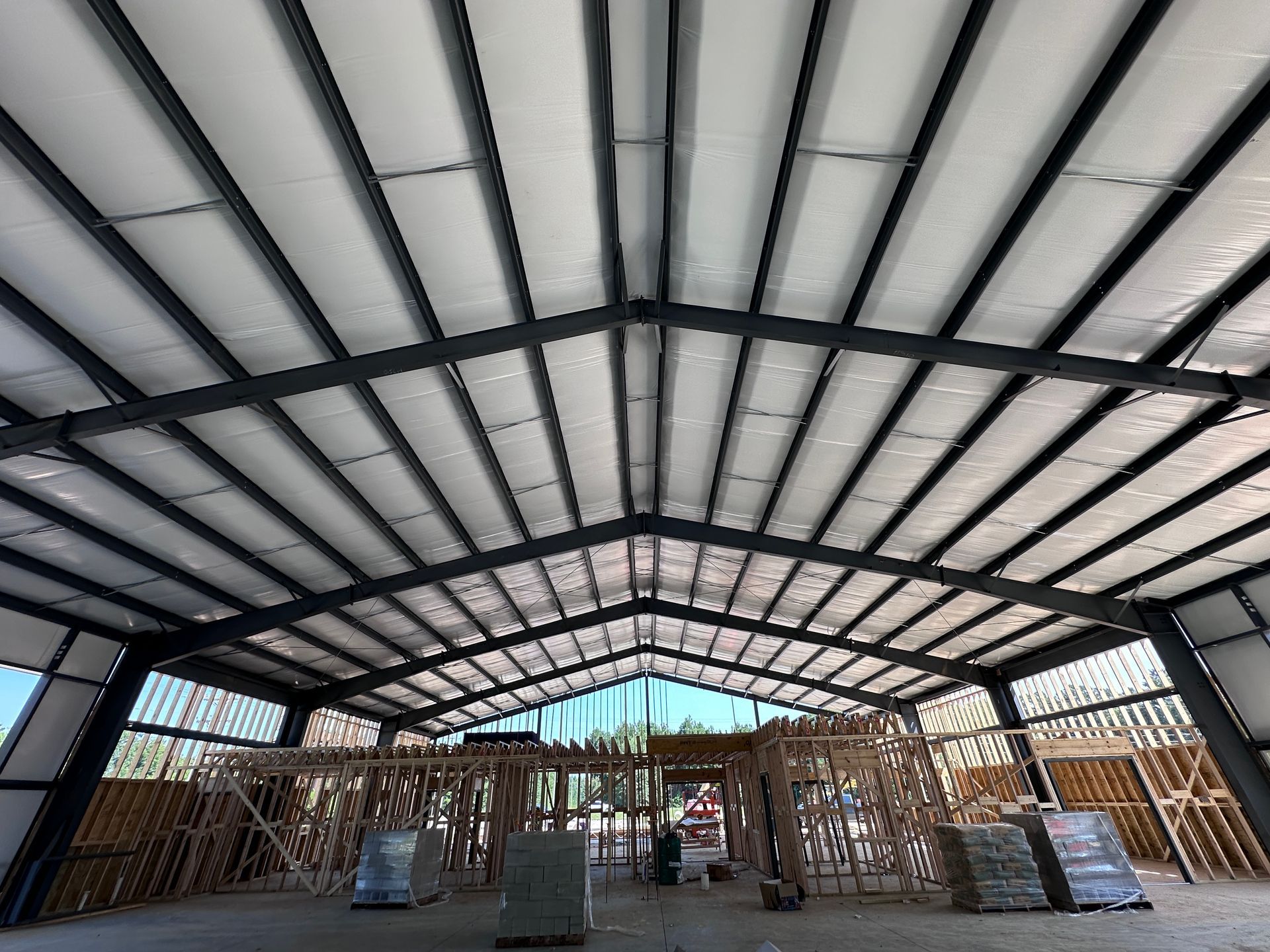 Interior of an empty metal-framed warehouse with a high arched roof and stacked materials at the sides