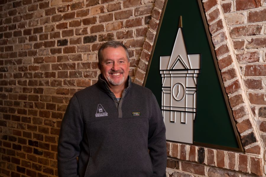 A man is standing in front of a brick wall with a clock tower on it.