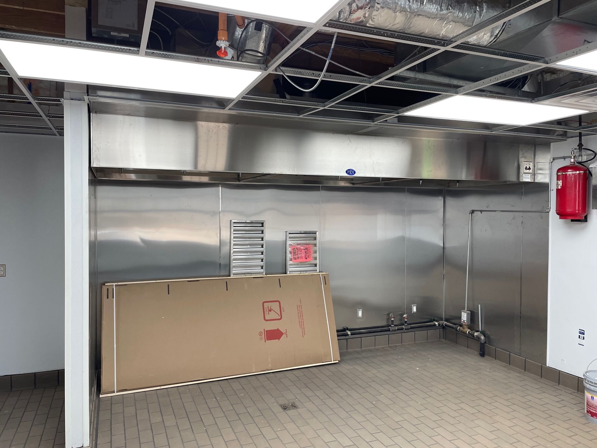 An empty room with stainless steel walls and a fire extinguisher hanging from the ceiling.