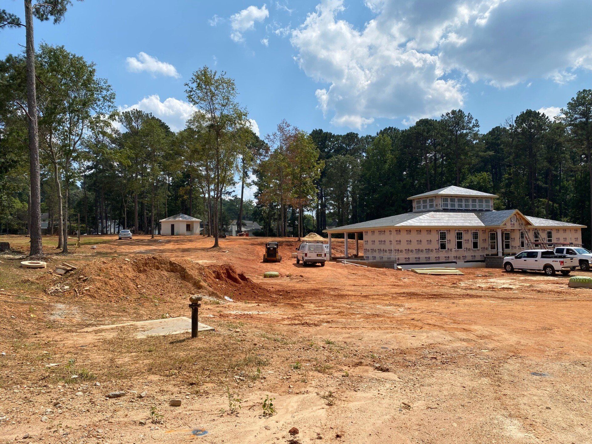 A house is being built in the middle of a dirt field surrounded by trees.