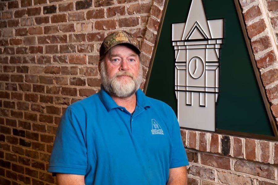 A man in a blue shirt and hat is standing in front of a brick wall.