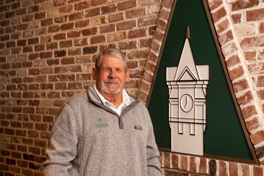 A man is standing in front of a brick wall with a clock tower on it.