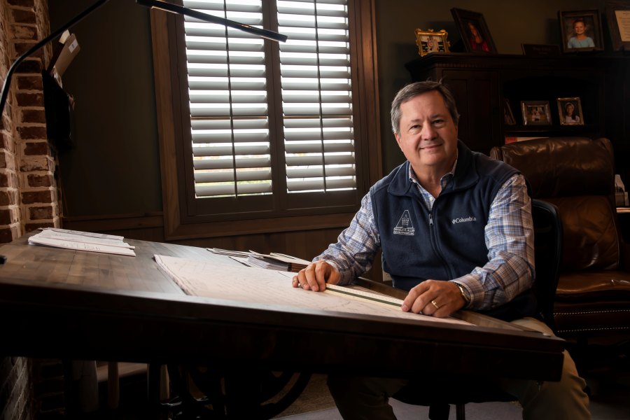 A man is sitting at a desk in a room with shutters on the windows.