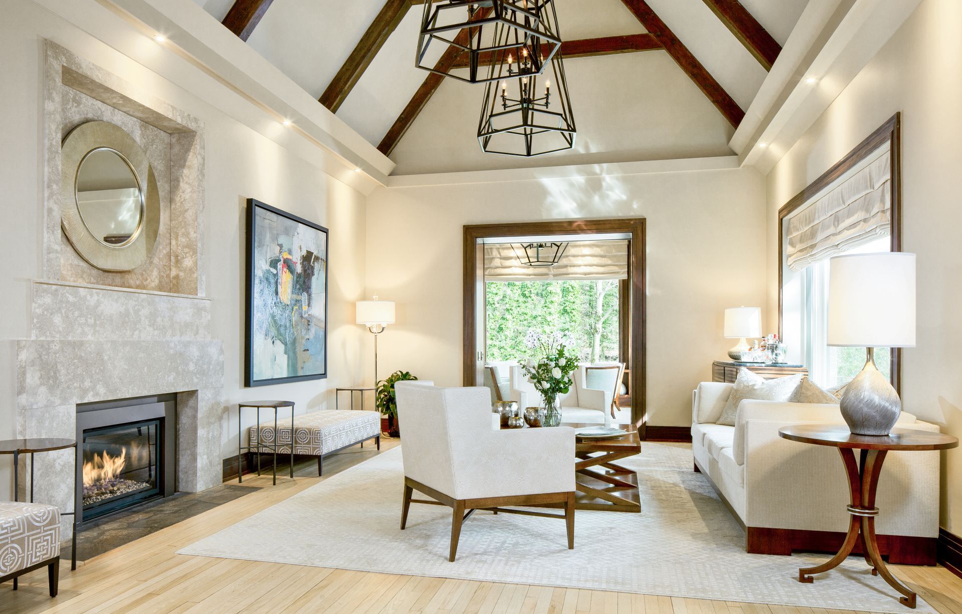 Living room with fireplace, neutral colors, light wood floors, and large windows overlooking a green view.