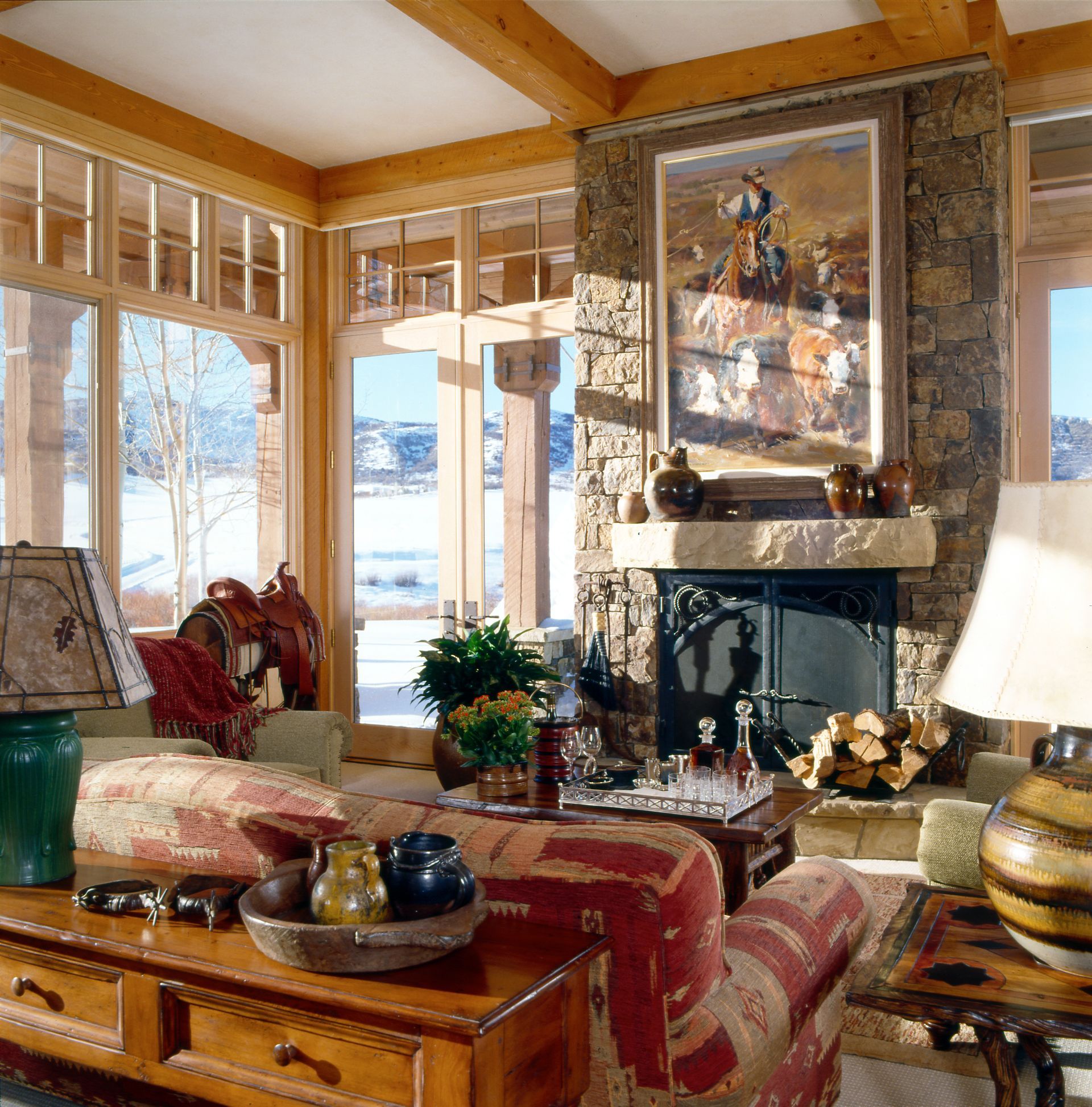Cozy living room with leather chairs, stone fireplace, large windows overlooking a lake.
