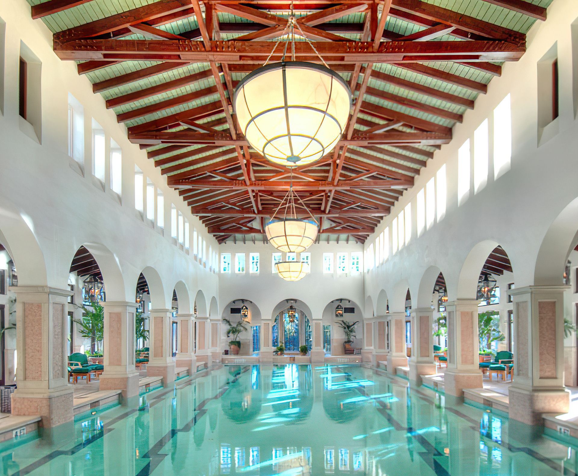 Indoor swimming pool with arches, columns, wood beam ceiling, and hanging globe lights.