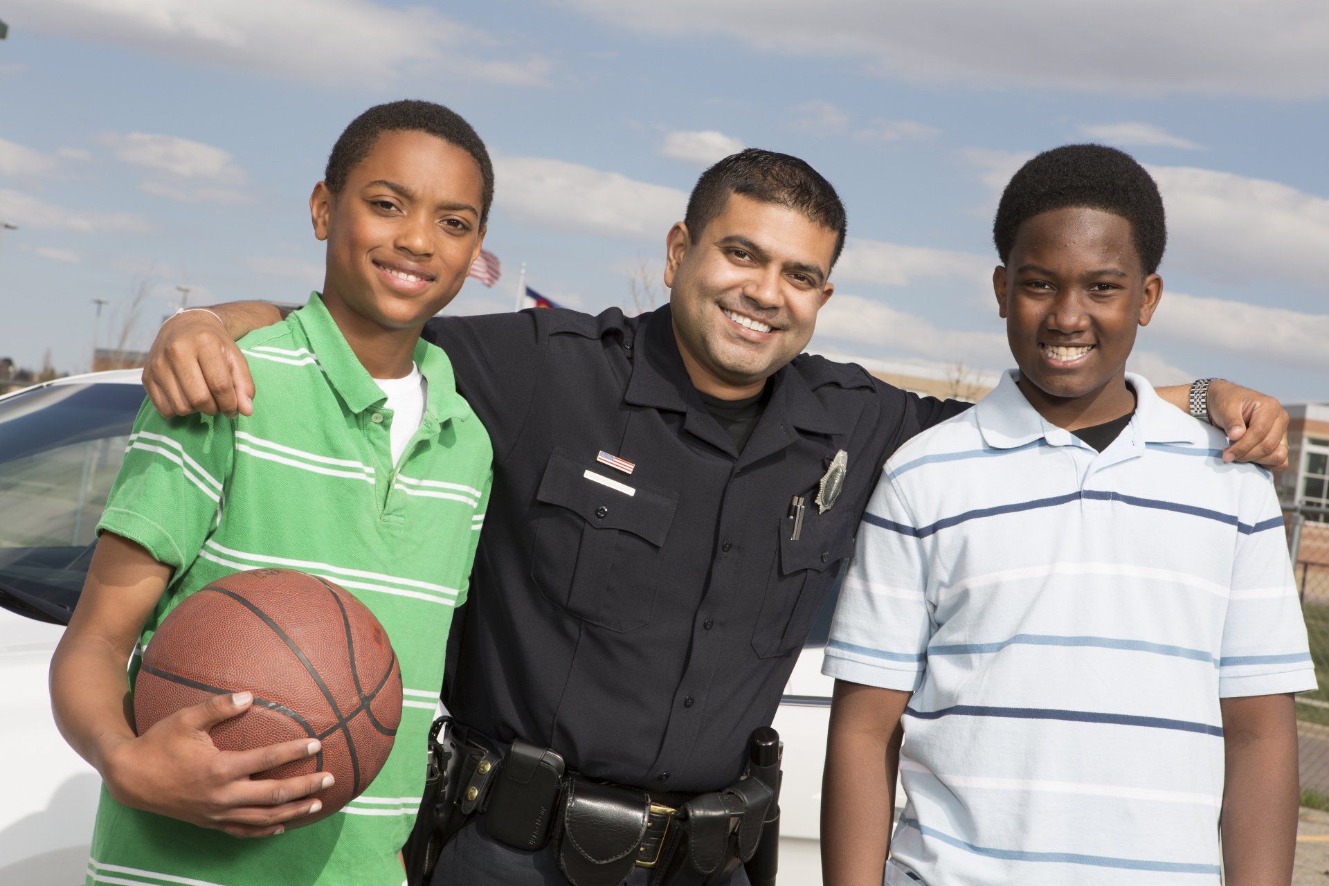 A police officer is posing for a picture with two boys one of whom is holding a basketball