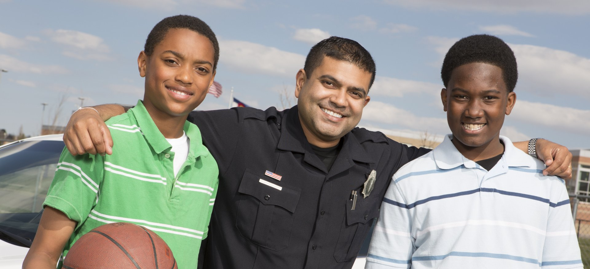 A police officer is posing for a picture with two boys and a basketball.