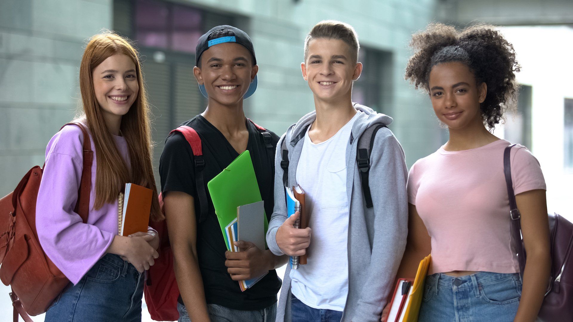A group of young people standing next to each other holding books and backpacks.