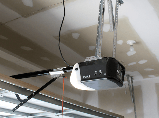 Garage door opener mounted to the ceiling in a garage, with rails and hanging cords.