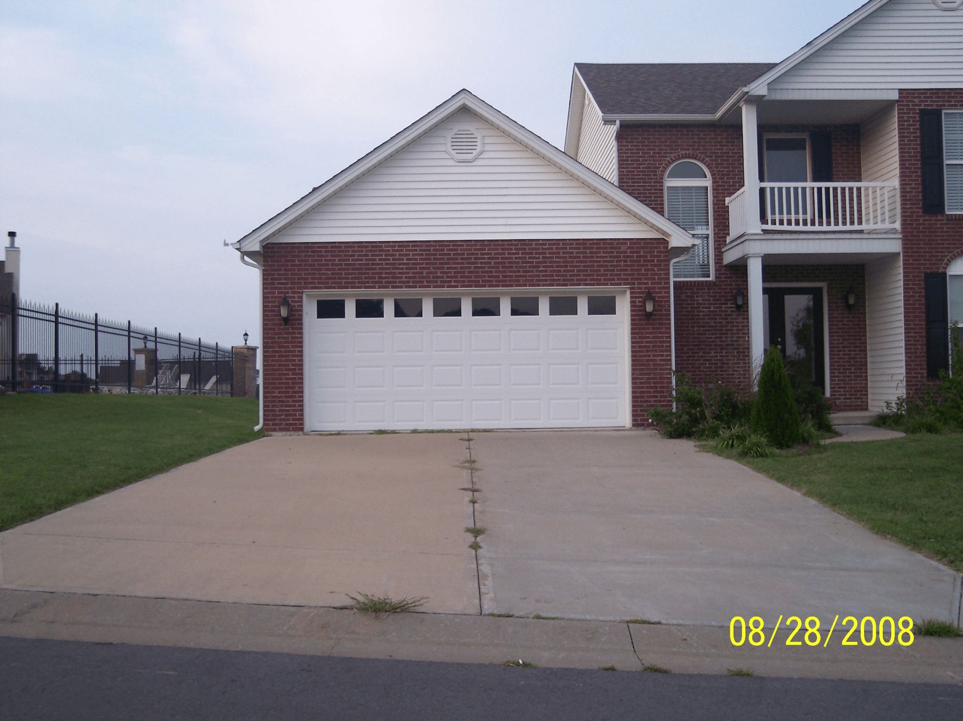 Brick house with white garage doors and a large driveway under a cloudy sky