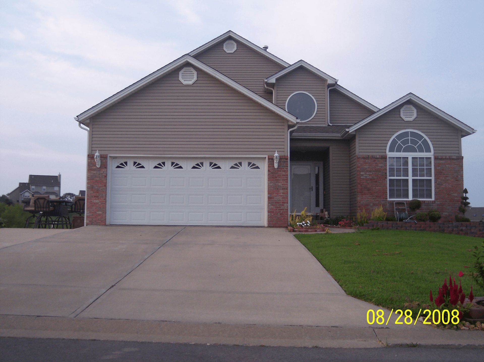 Suburban house with beige siding, white garage door, driveway, and green lawn