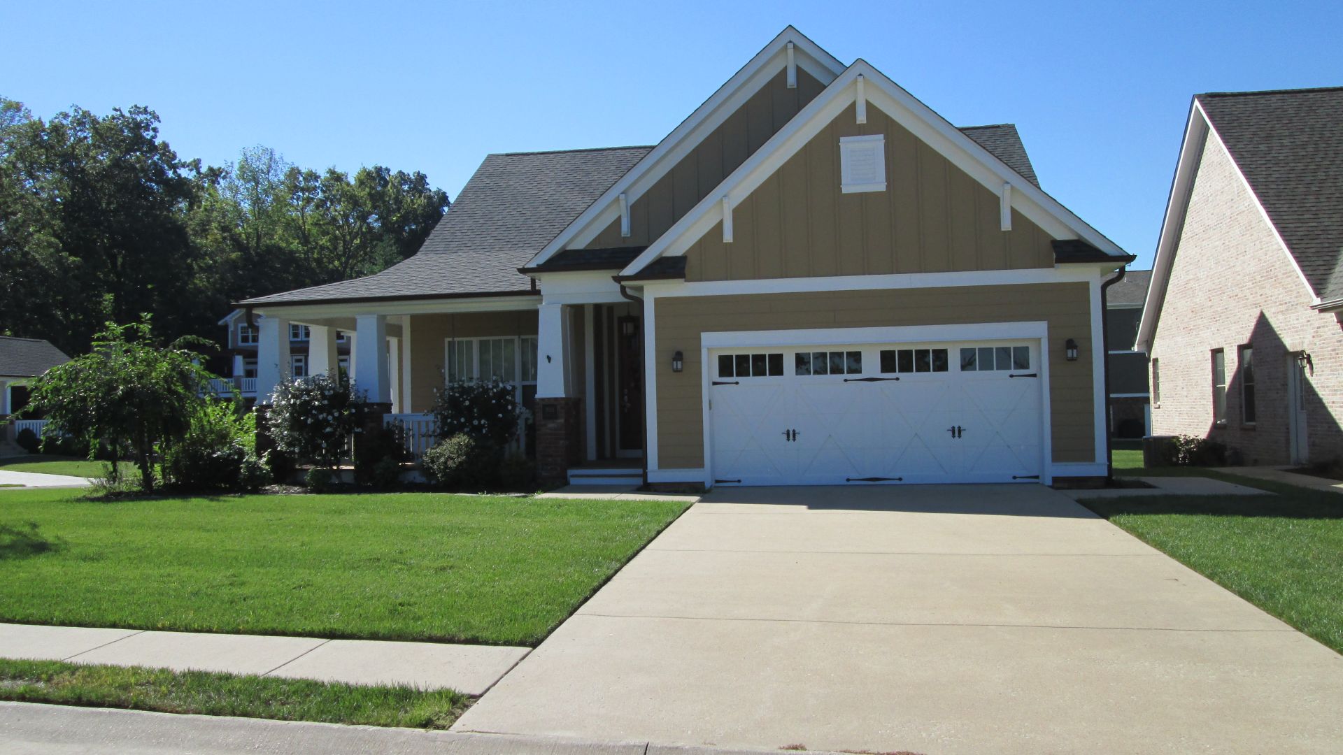 Suburban house with a white garage door, tan siding, and a green lawn beside a driveway