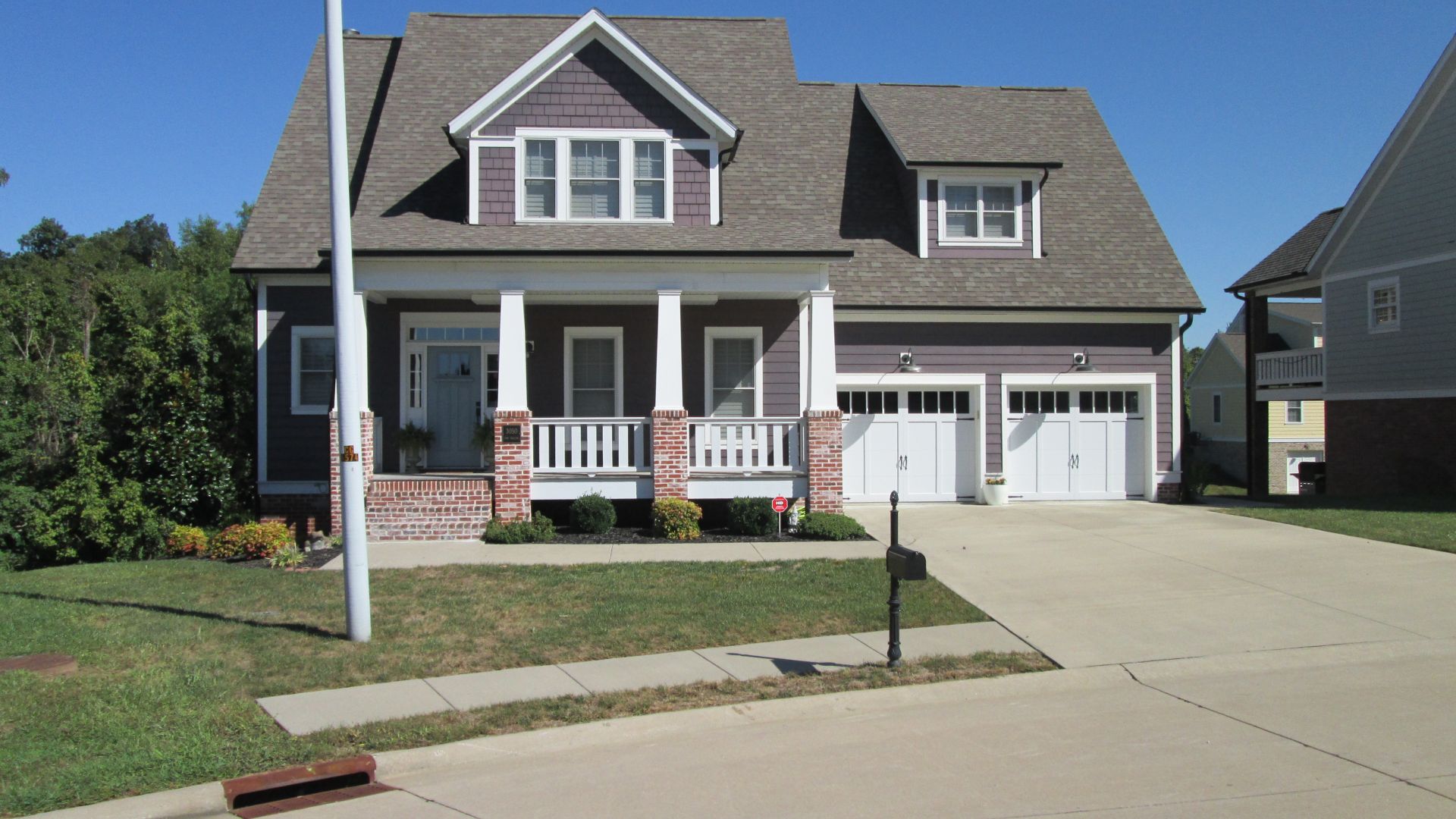 Suburban two-story house with brick porch, garage, and a driveway on a sunny day