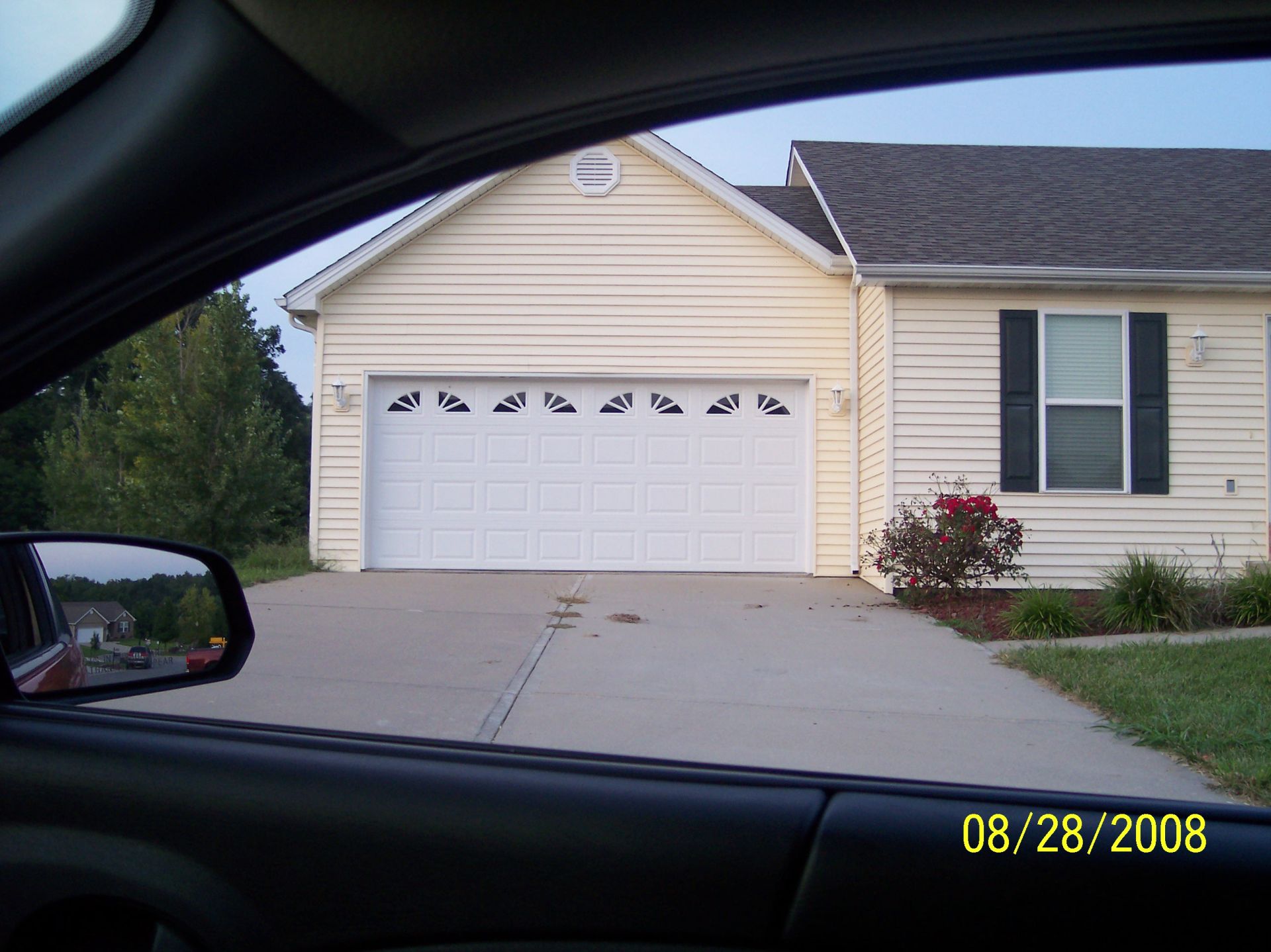 View from a car of a beige house with a white garage door and driveway, dated 08/28/2008.