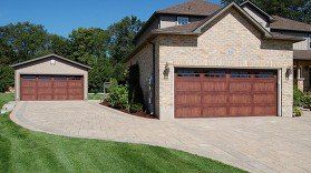 Two brick houses with attached garages and a curved driveway under a clear blue sky