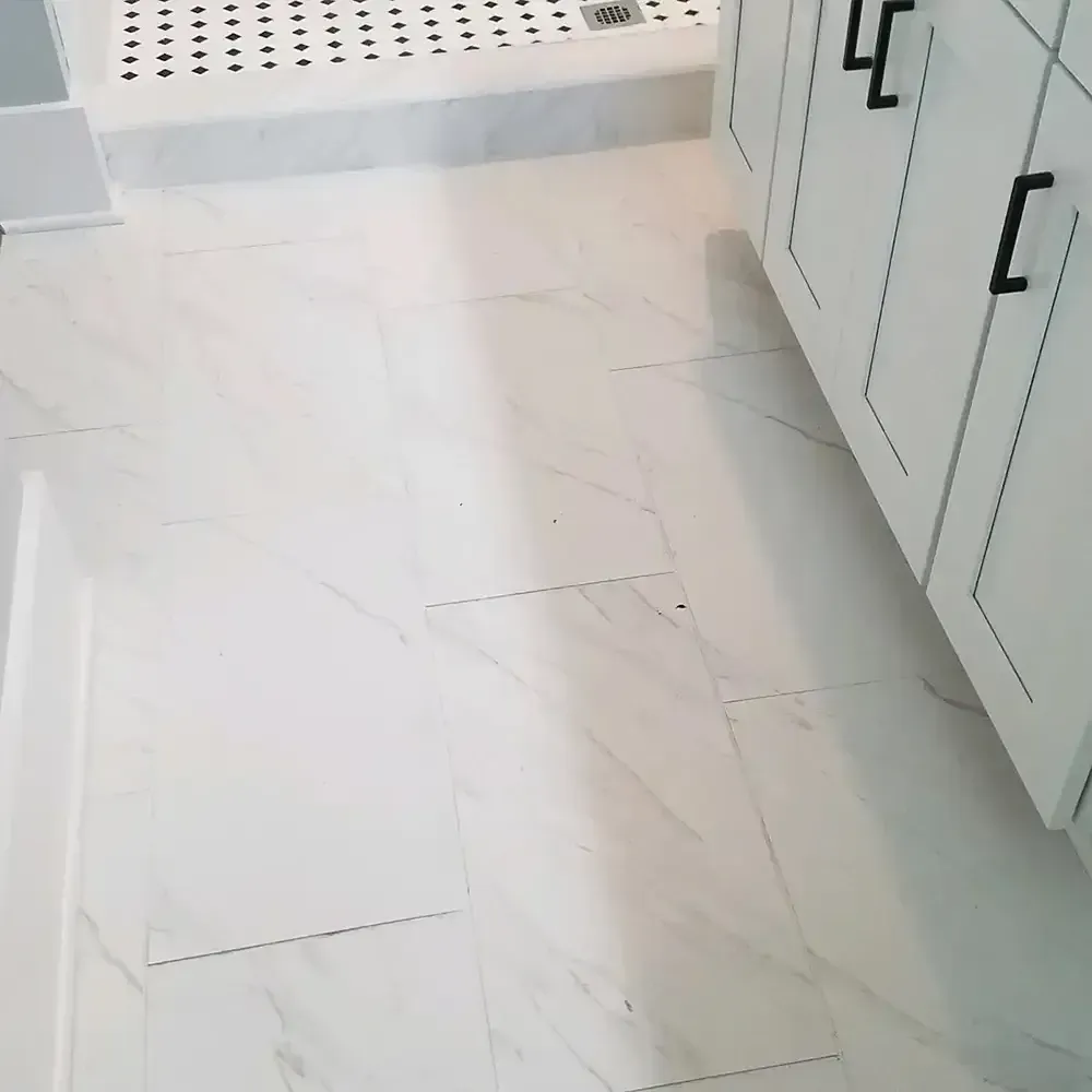 White marble bathroom floor with a white shower and cabinets with black hardware.