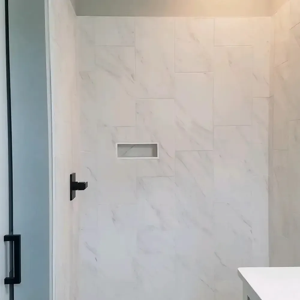 A modern shower with white marble-look tiles, a built-in shelf, and black hardware. The shower is clean and bright.