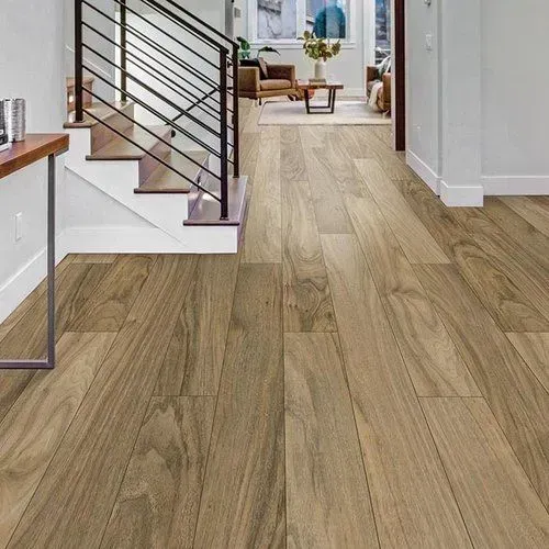 Wooden flooring in a hallway with a staircase to the left, leading to a living area with furniture.