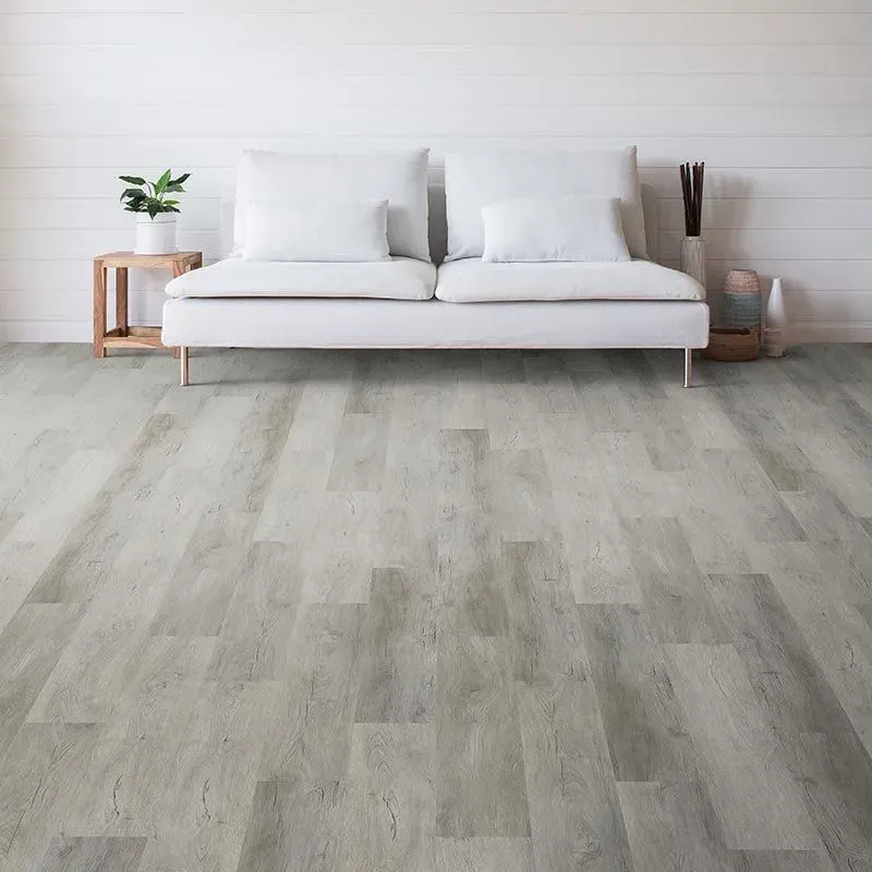 A modern living room with light gray wood-look flooring and a white couch against a white shiplap wall.