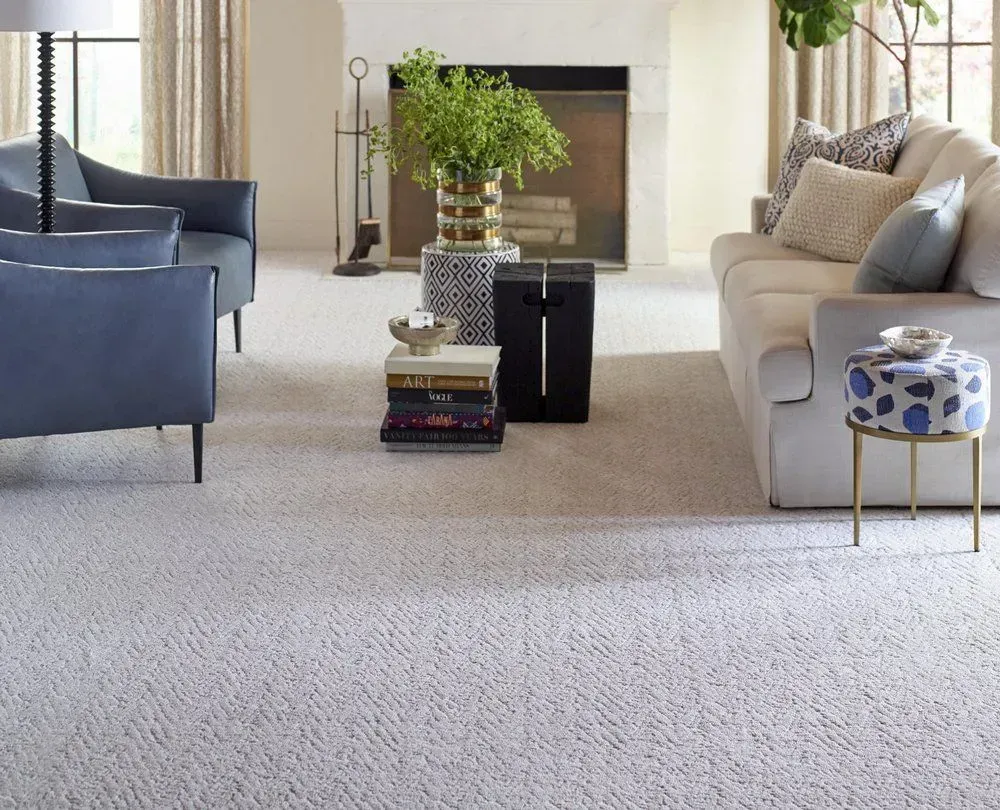 A living room with neutral carpet, blue armchairs, a cream sofa, and a fireplace in the background.