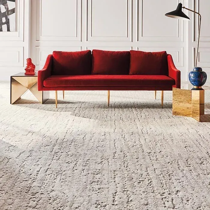 Red velvet sofa in a living room with a textured rug, flanked by gold accent tables and decor.