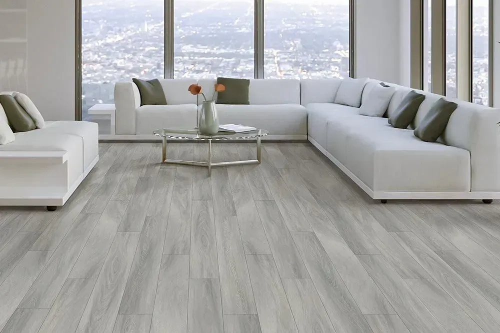 A modern living room with light gray wood-look flooring and a white sectional sofa near large windows with a city view.