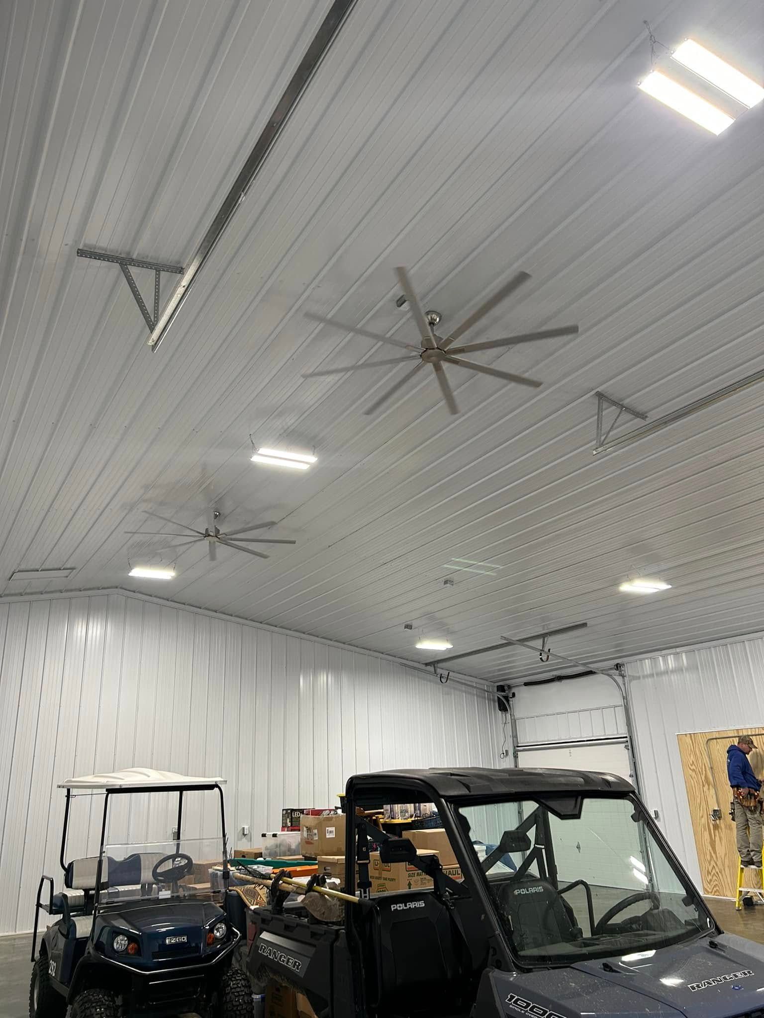 Indoor garage with several utility vehicles under a white ceiling with large fans and bright lights