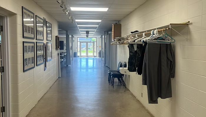 Long indoor hallway with framed photos on the left and coats hanging on racks on the right.