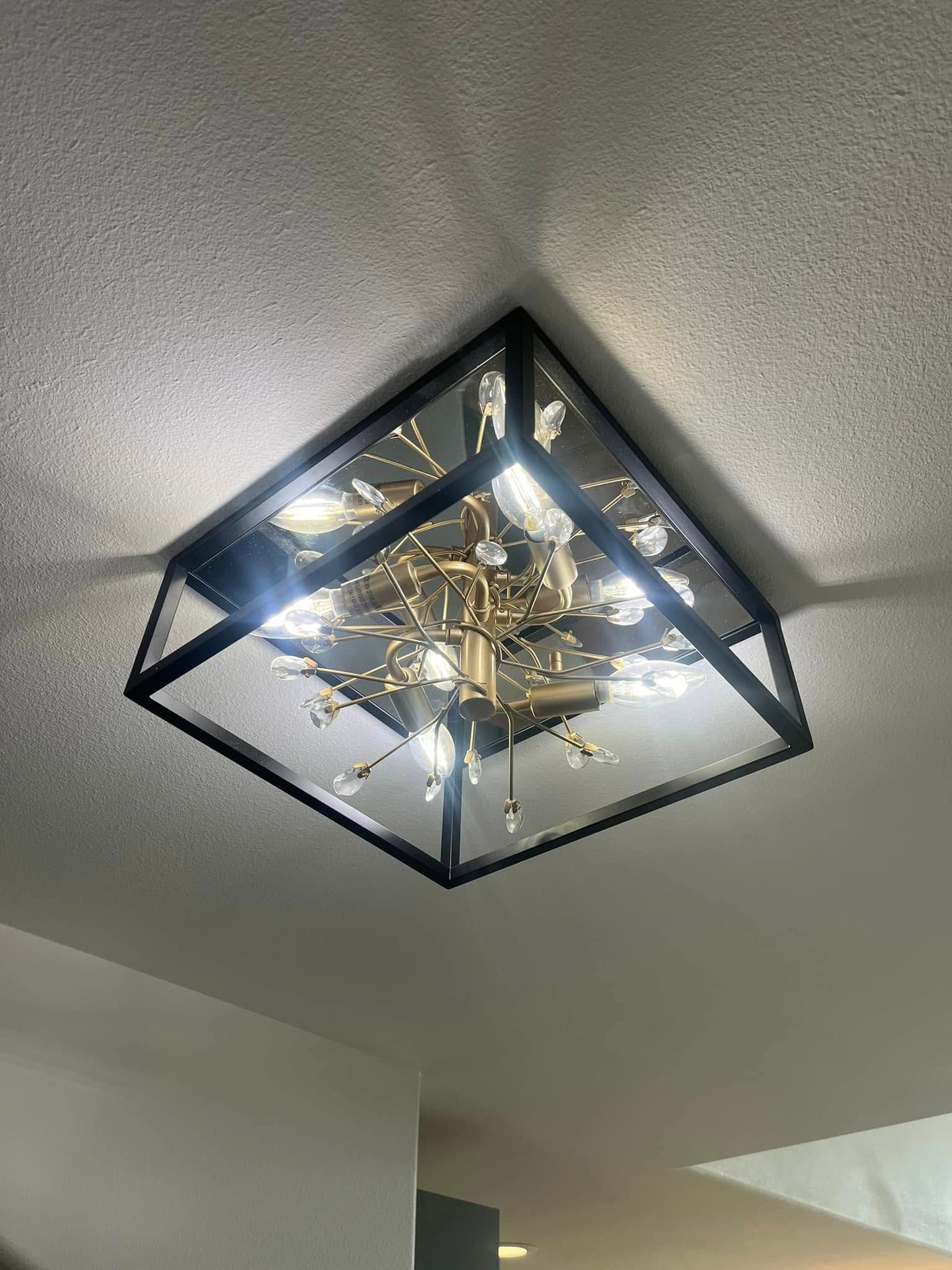 Geometric black ceiling light fixture with bright gold-toned bulbs on a white ceiling