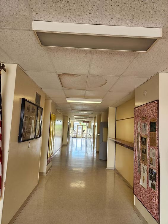 Long, empty hallway with beige walls, fluorescent ceiling lights, and bulletin boards on both sides.