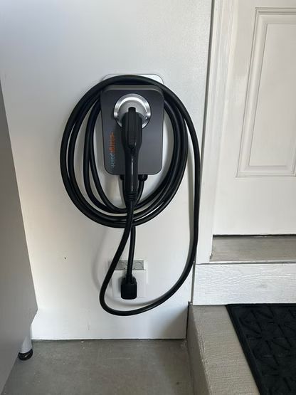 Wall-mounted EV charging cable coiled on a gray panel beside a door.