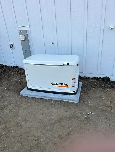 White Generac generator on a concrete pad beside a house wall outdoors.