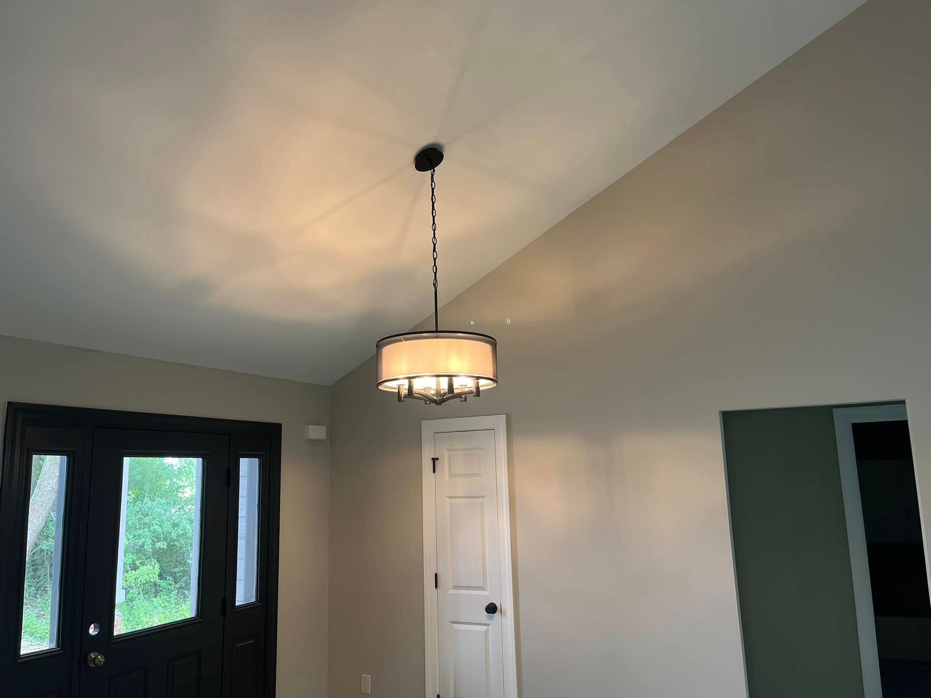 Interior room with vaulted ceiling, hanging light fixture, white door, and black double doors with windows